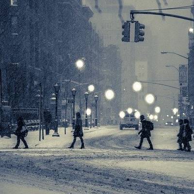 Pedestrians crossing snowy city street at night.